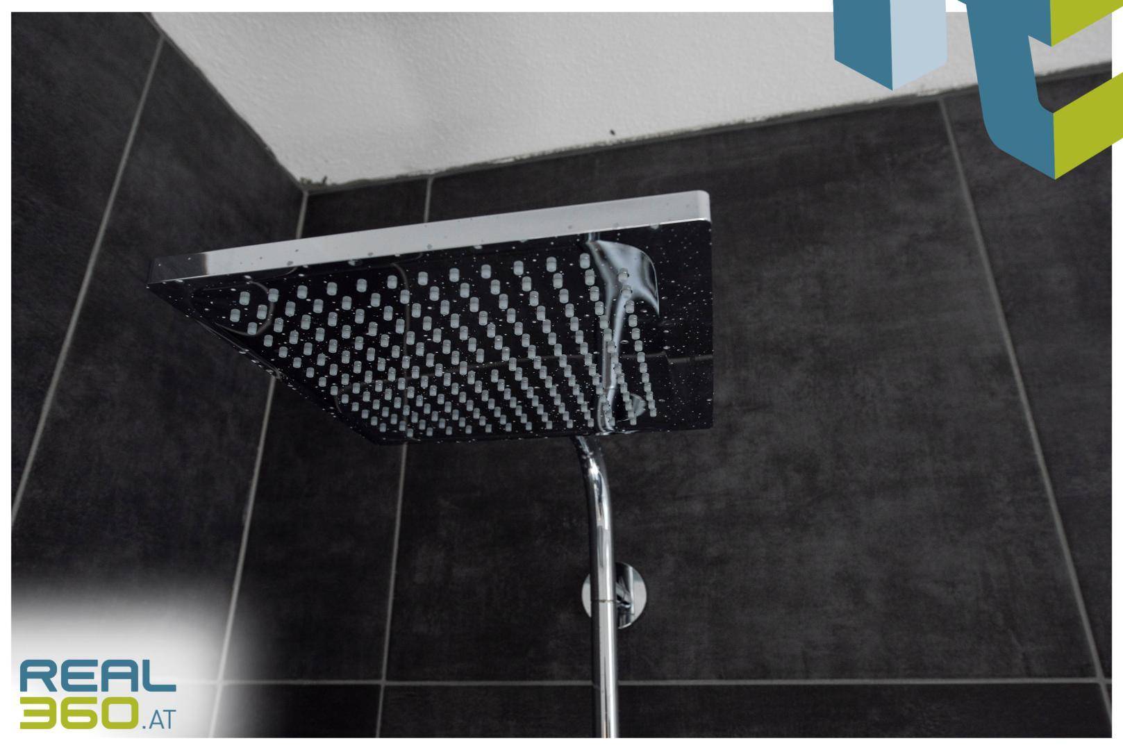 Detailaufnahme einer modernen Regendusche mit dunklen Wandfliesen.