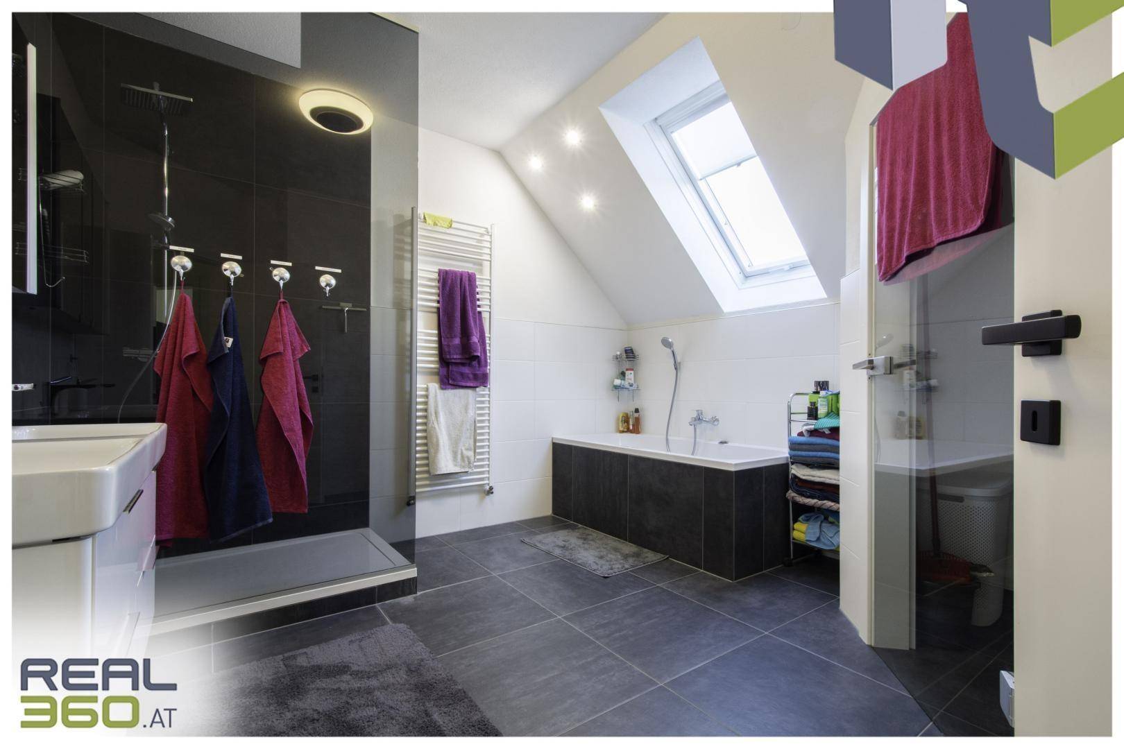 Modernes Badezimmer mit dunklen Fliesen, Badewanne und Dachfenster.