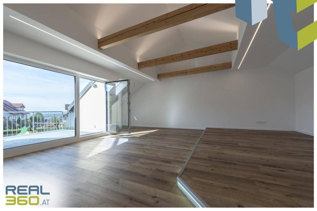 Heller Wohnraum mit großen Fenstern, Holzbalken und Zugang zu einem Balkon.