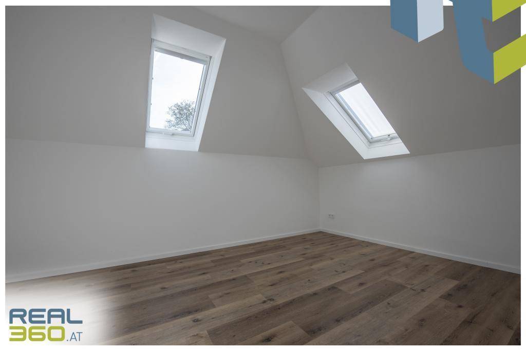 Helles Schlafzimmer mit zwei Dachfenstern und Holzboden.