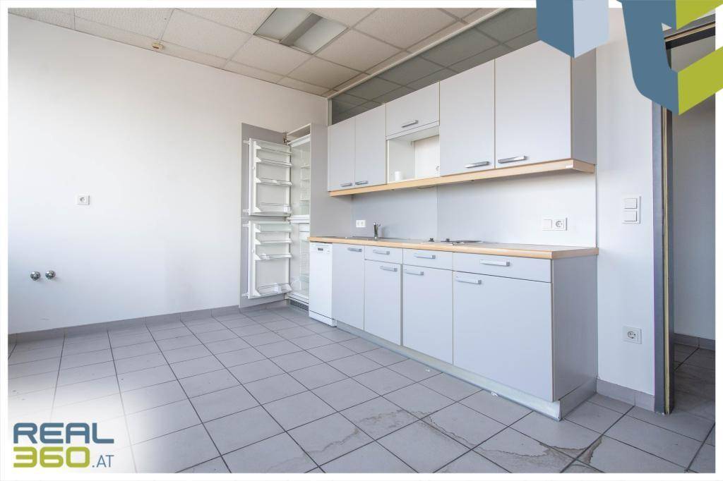 Kleine Küchenzeile mit weißen Schränken, Spüle und Kühlschrank, ideal für Pausenbereiche.