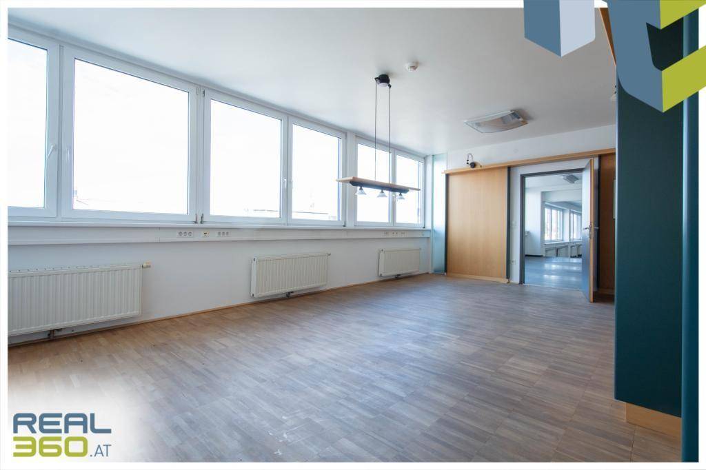 Heller Büroraum mit Holzboden und großen Fenstern, die viel Tageslicht hereinlassen.