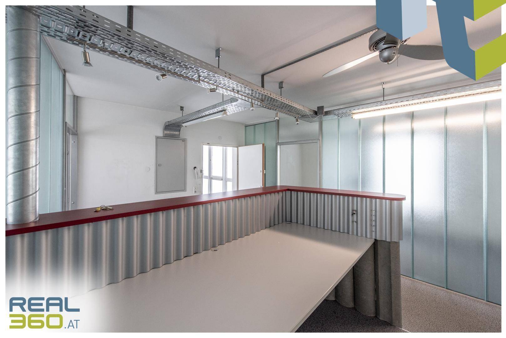 Moderner Bürobereich mit einer langen Theke, Glaswänden und sichtbaren Installationen an der Decke.