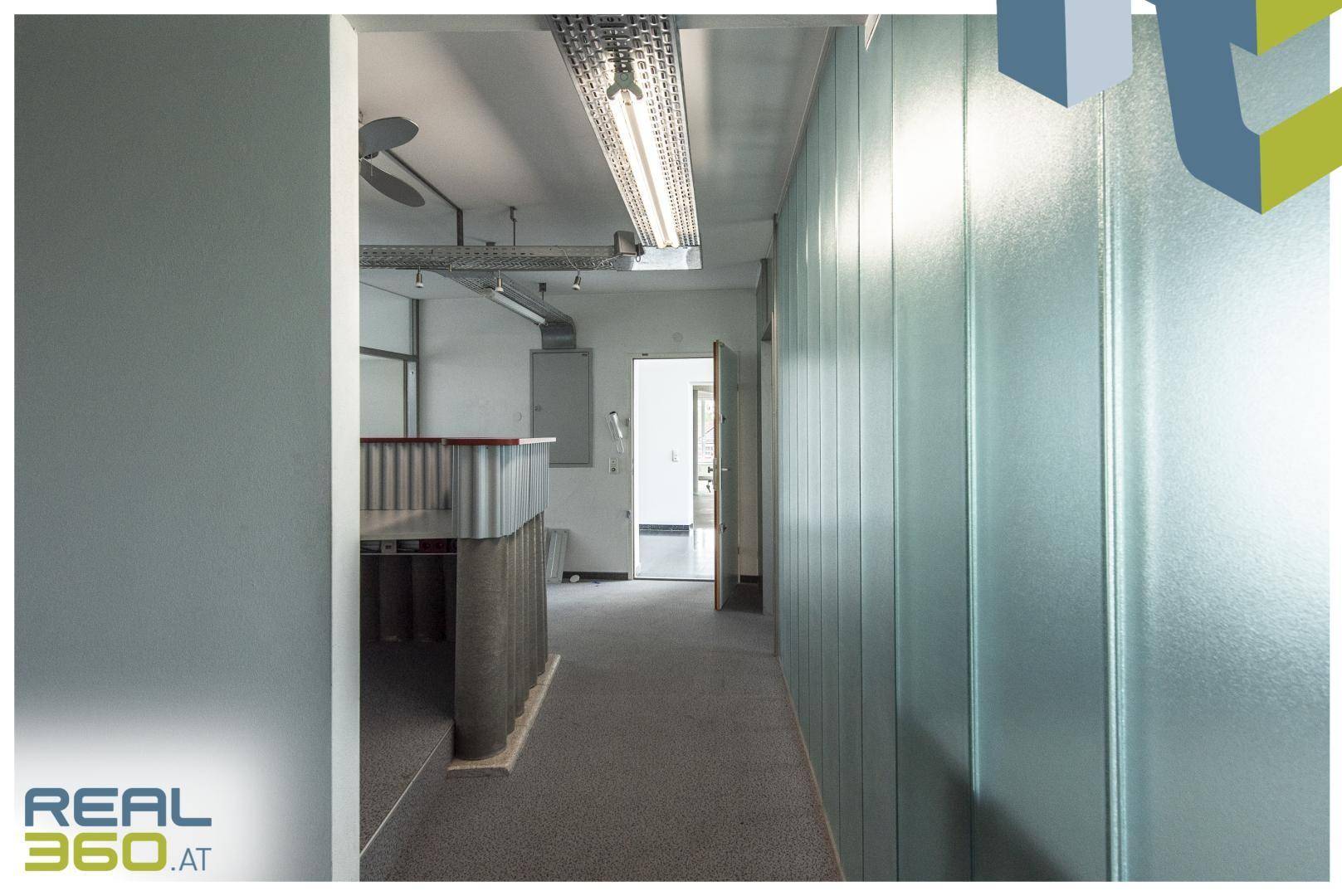 Flur in einem Bürogebäude mit Glaswänden, Teppichboden und Blick auf den Empfangsbereich.