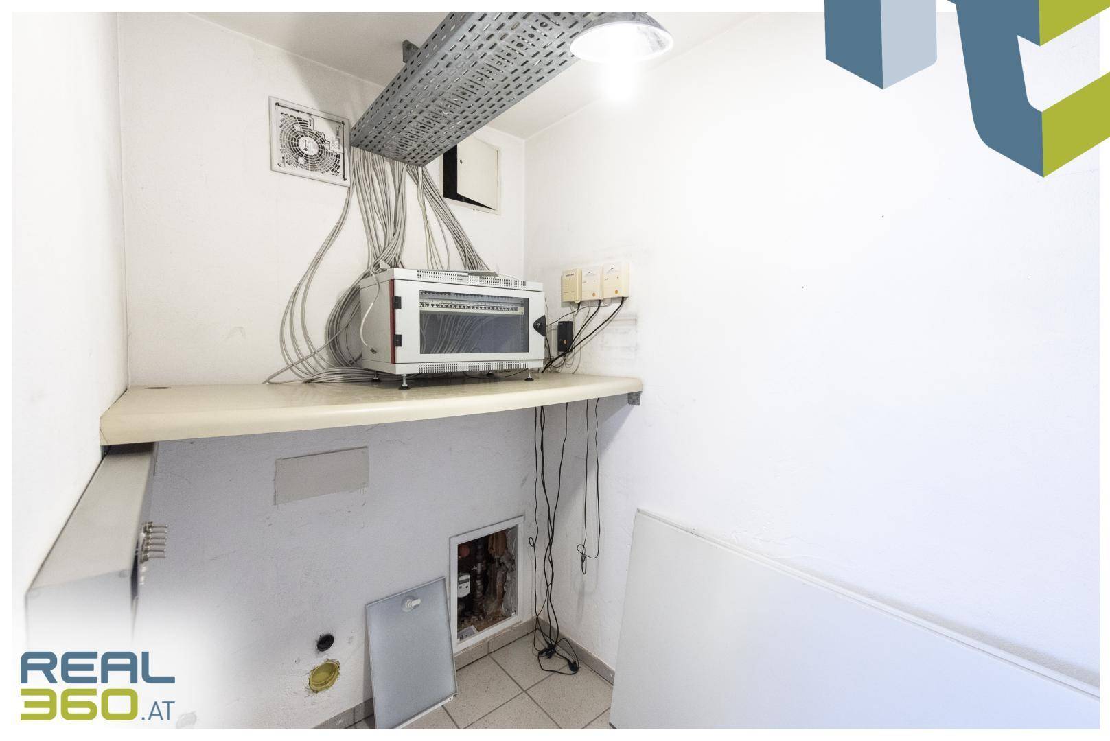 Technikraum mit sichtbaren Kabeln, Serverrack und einer Arbeitsplatte.