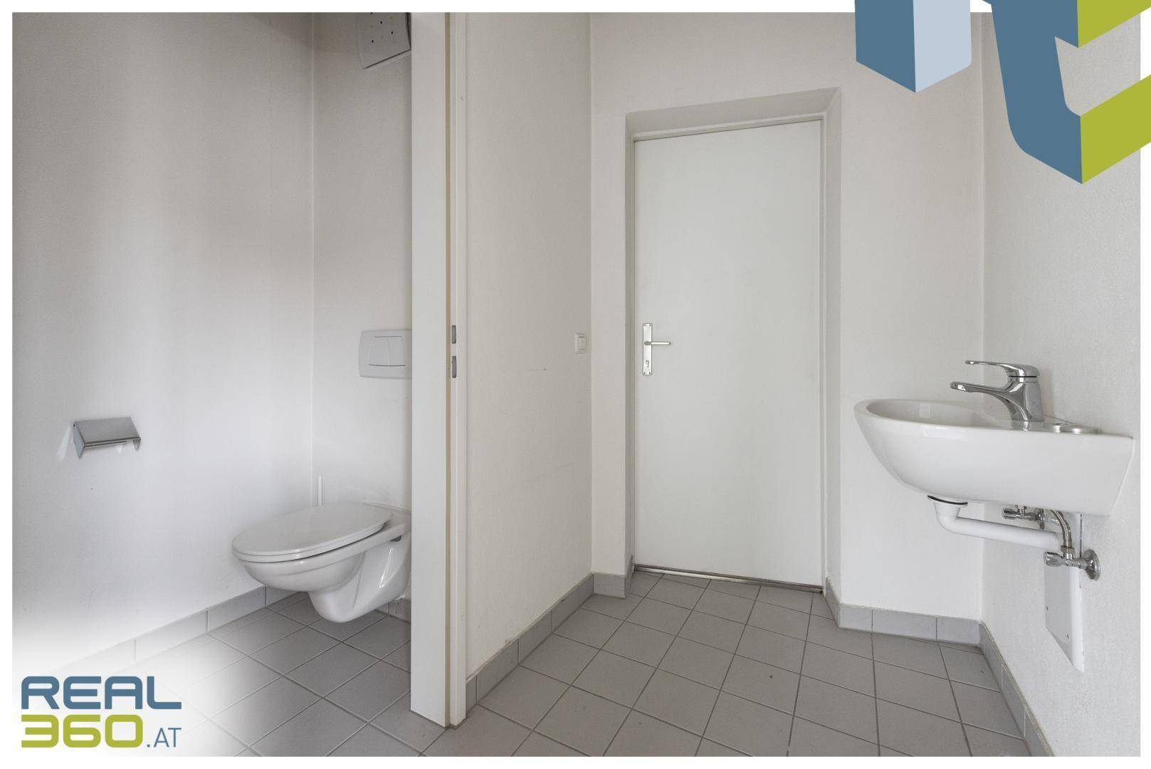 Helle Gästetoilette mit Wand-WC, kleinem Waschbecken und grauen Fliesen.