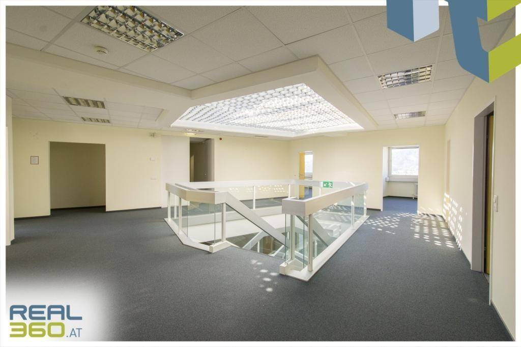 Offener Bürobereich mit moderner Treppe, Glasgeländer und großer Deckenbeleuchtung.