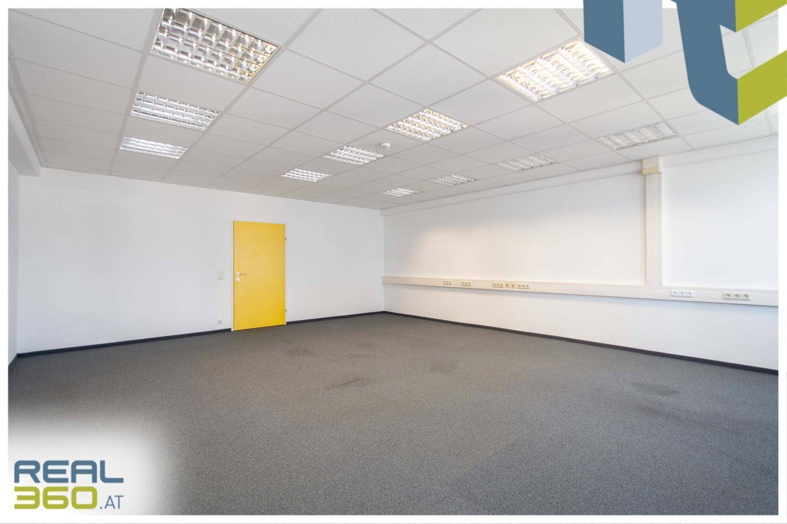 Großes, leeres Büro mit Teppichboden, weißen Wänden und einer leuchtend gelben Tür.