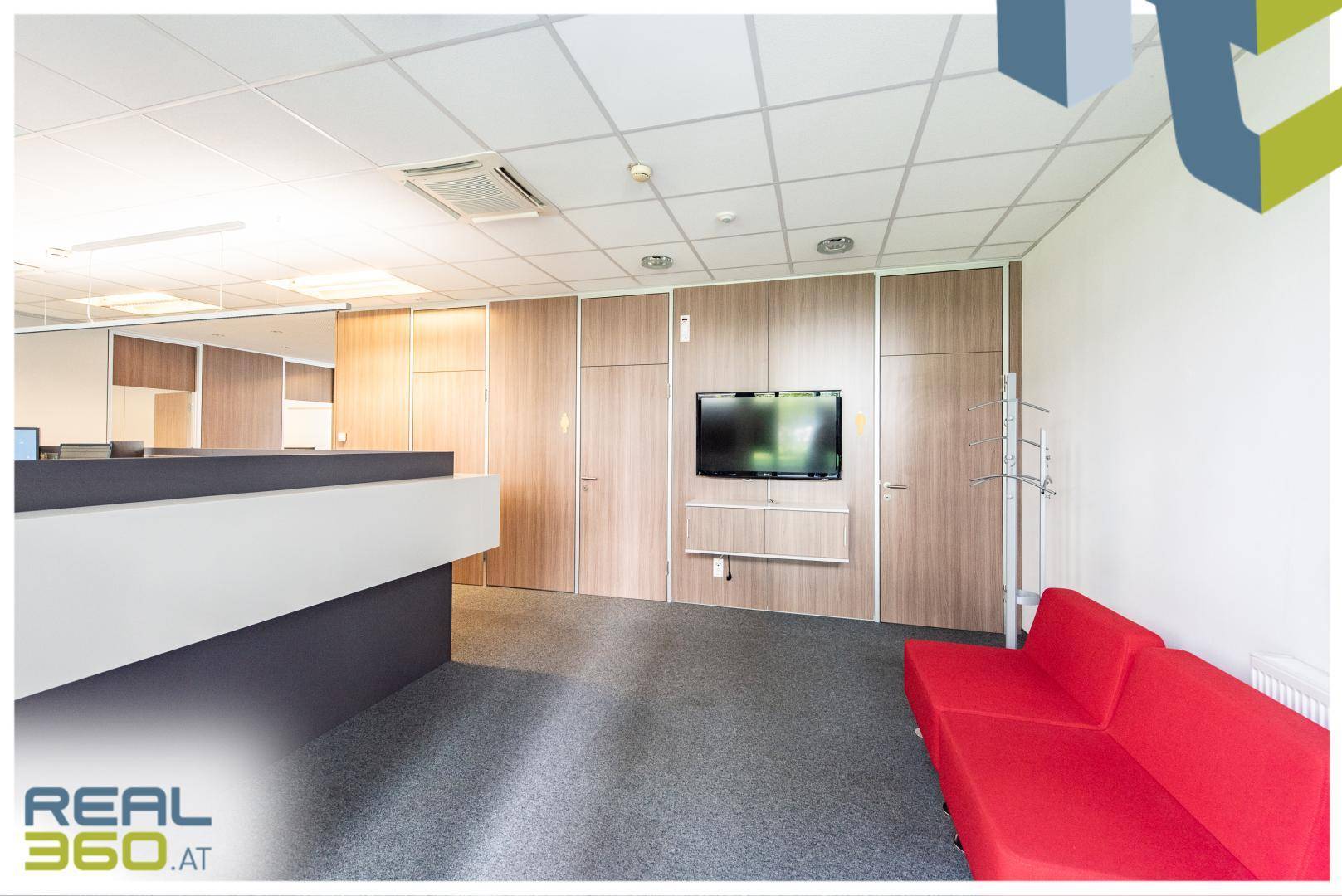 Empfangsbereich eines Büros mit rotem Sofa, Wandfernseher und Holzverkleidung, ideal für Wartezonen.