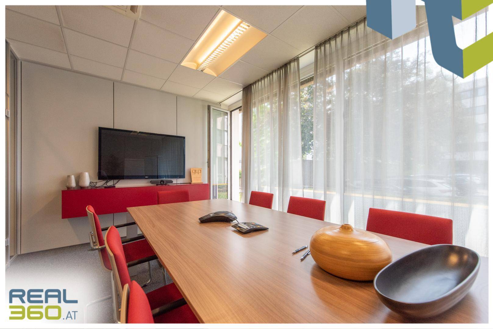 Konferenzraum mit großem Holztisch, roten Stühlen und einem Wandfernseher, ideal für Besprechungen.