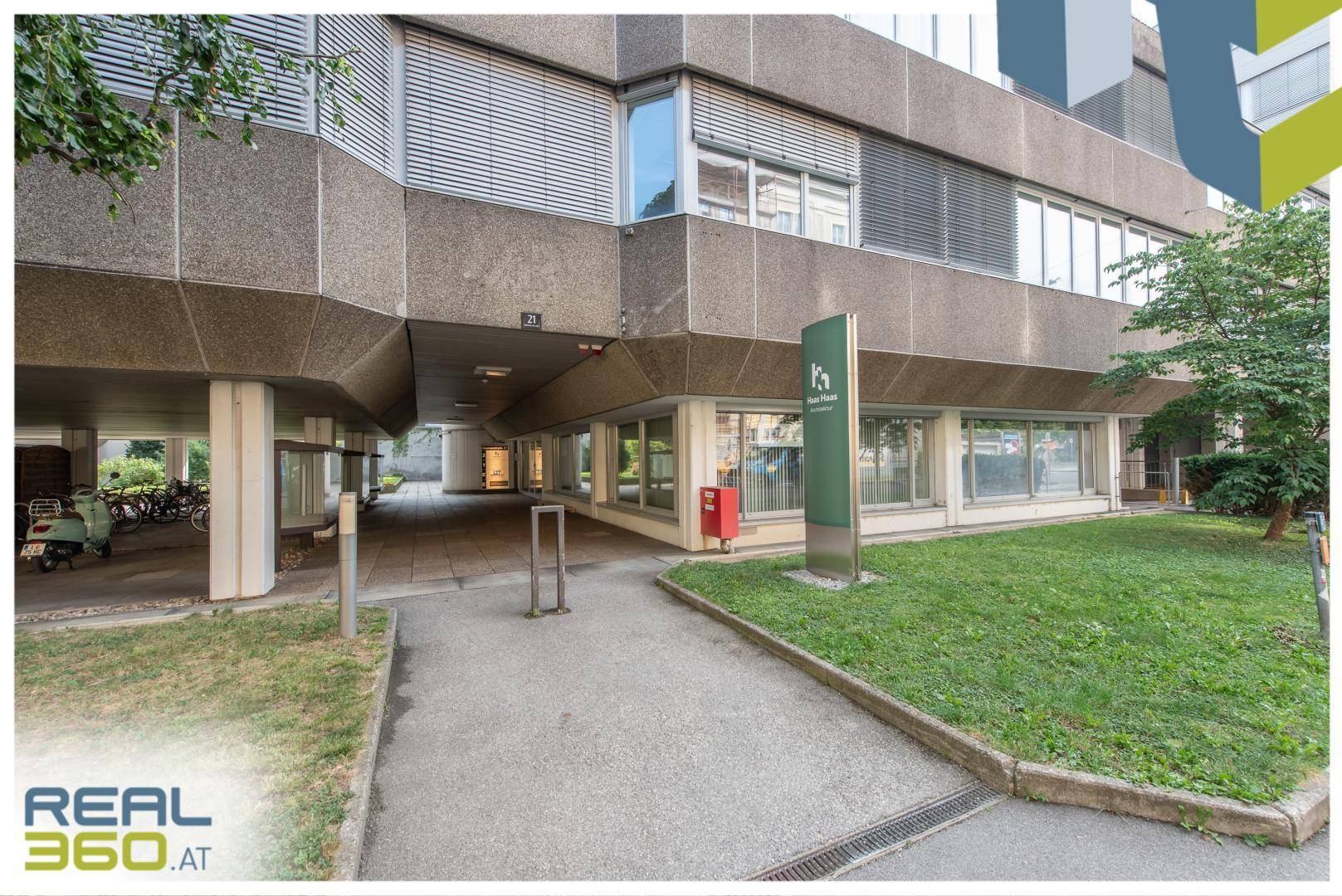 Außenansicht eines modernen Bürogebäudes mit Betonfassade, großen Fenstern und einer Grünfläche.