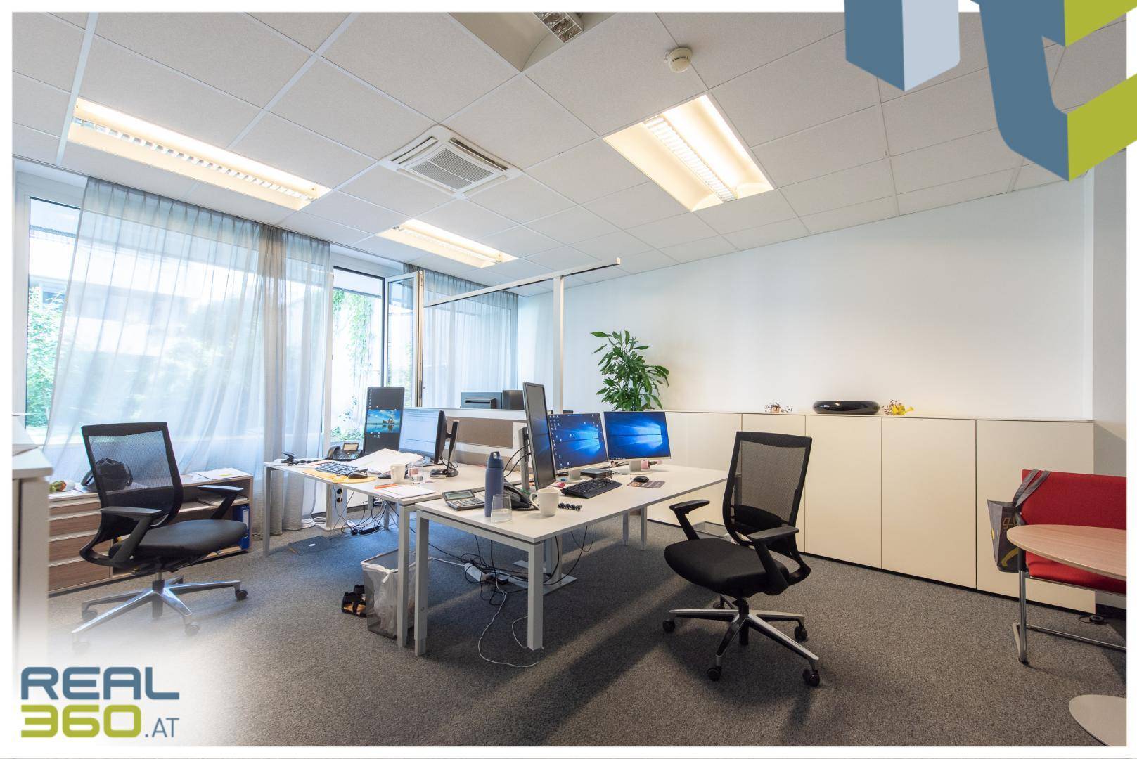 Offener Bürobereich mit mehreren Arbeitsplätzen, ergonomischen Stühlen und großen Fenstern für viel Licht.