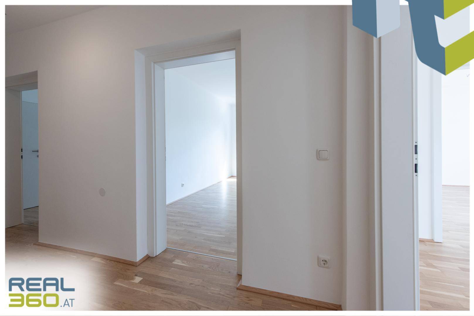 Übergangsbereich mit Parkettboden und weißen Wänden, der einen Blick in einen weiteren Raum ermöglicht.