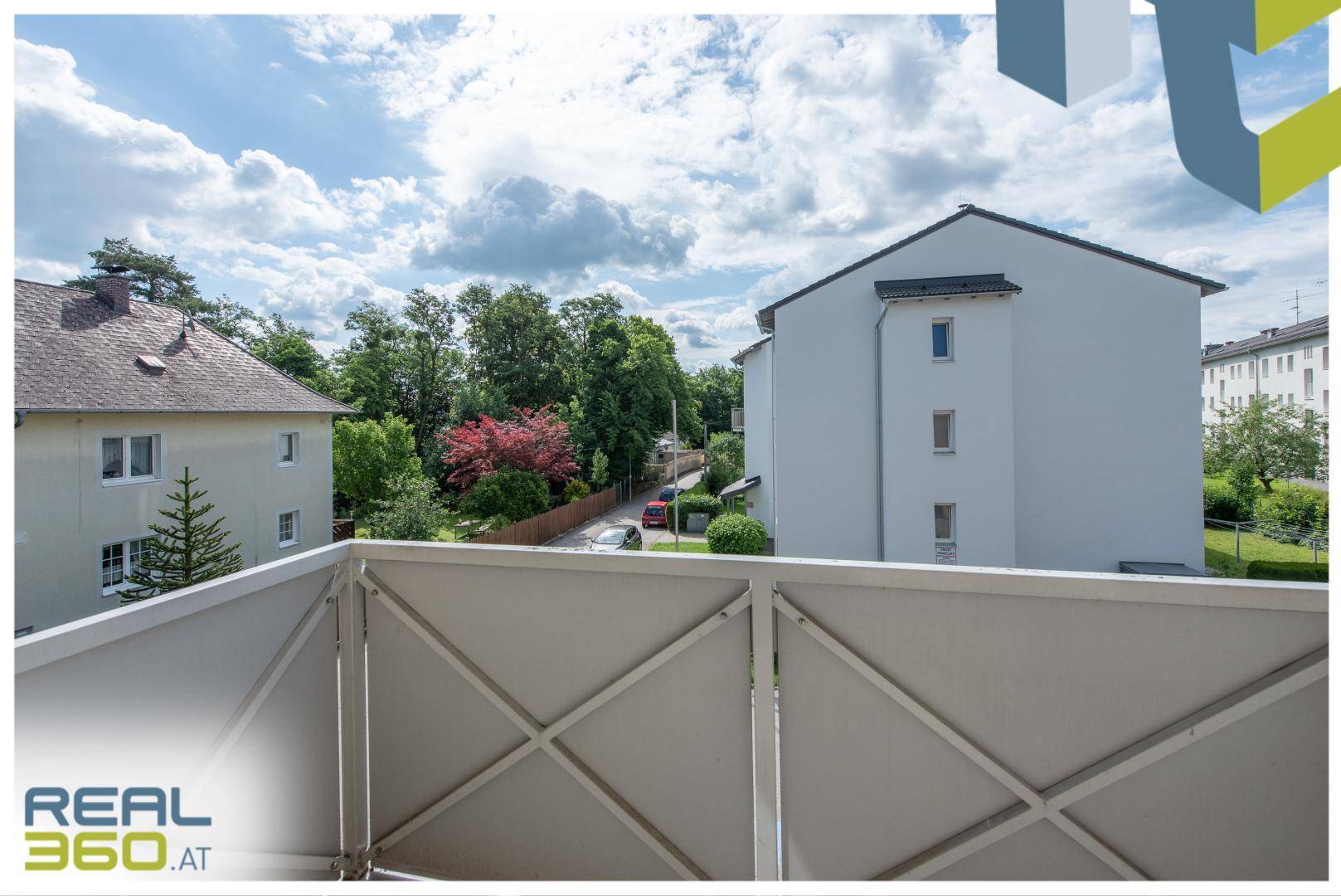 Ausblick von einem Balkon auf die umliegenden Gebäude, Bäume und eine ruhige Straße.