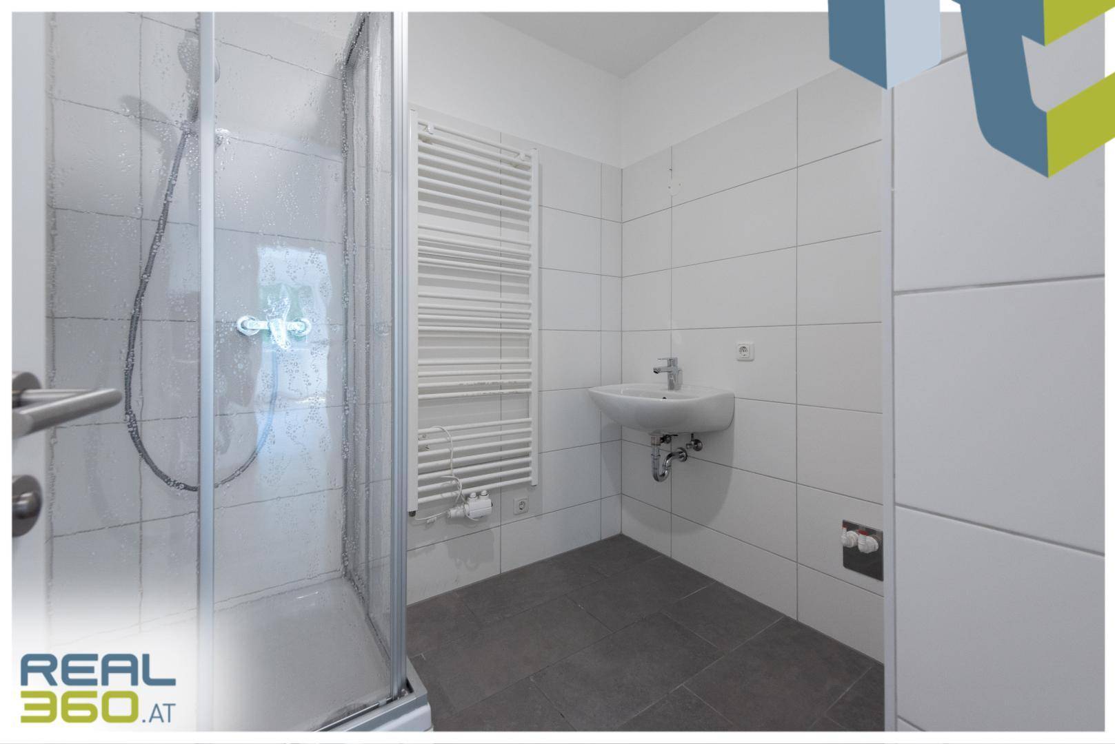 Modernes Badezimmer mit Duschkabine, Waschbecken und beheiztem Handtuchhalter in hellen Fliesen.