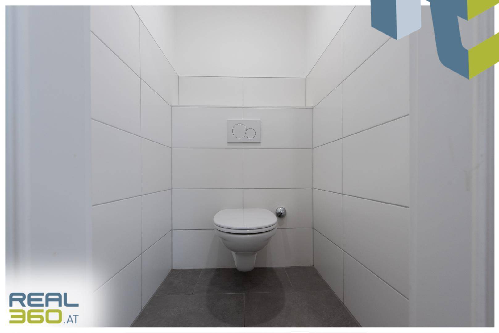 Separates WC mit wandhängender Toilette und modernen weißen Fliesen an den Wänden.