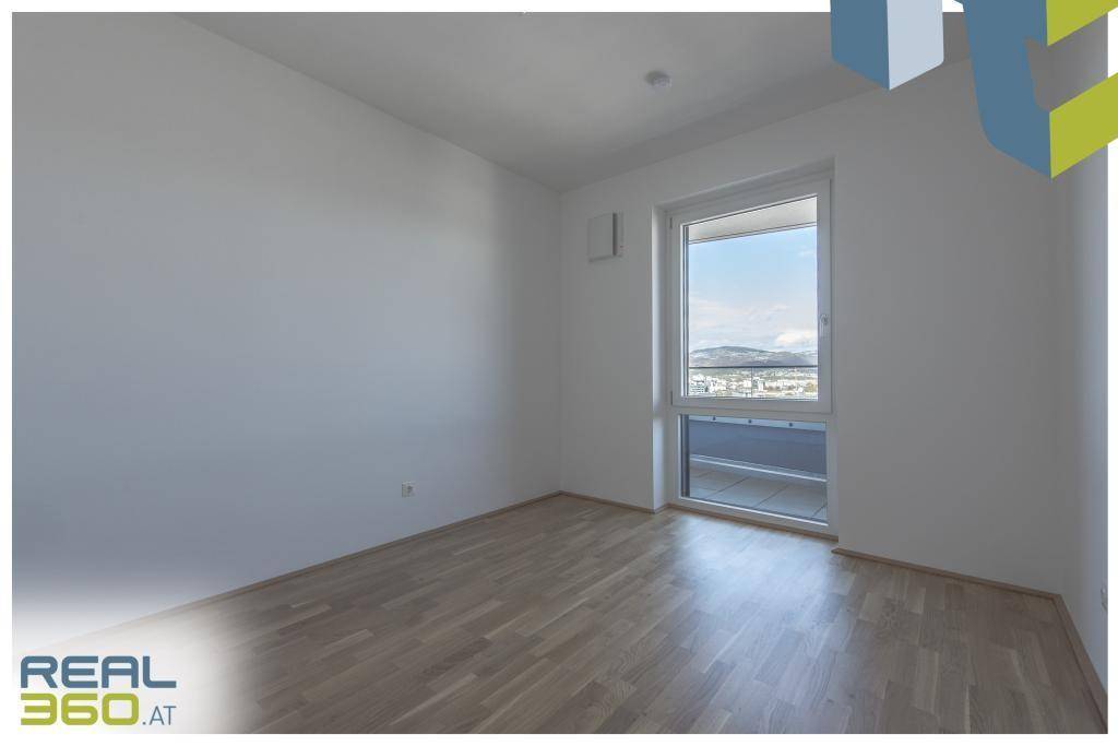 Helles Zimmer mit Parkettboden und Fenster, das einen weiten Blick über die Stadt bietet.