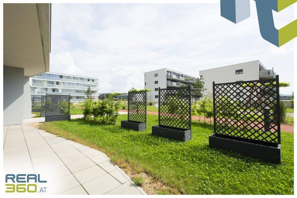 Gepflegter Gartenbereich mit Rasen, dekorativen Rankgittern und umliegenden Wohngebäuden.