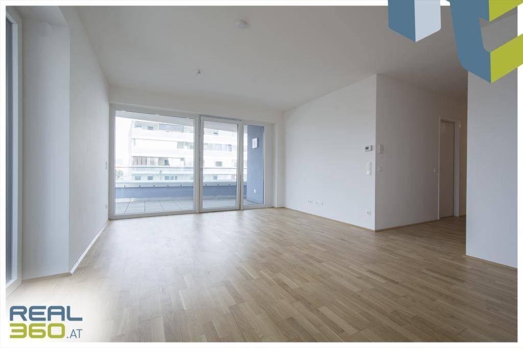 Heller, leerer Wohnraum mit Parkettboden und großen Schiebetüren zum Balkon.