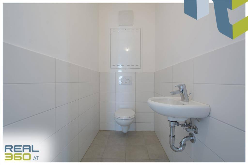 Kleines Gäste-WC mit weißen Fliesen, wandhängendem WC und kompaktem Eckwaschbecken.