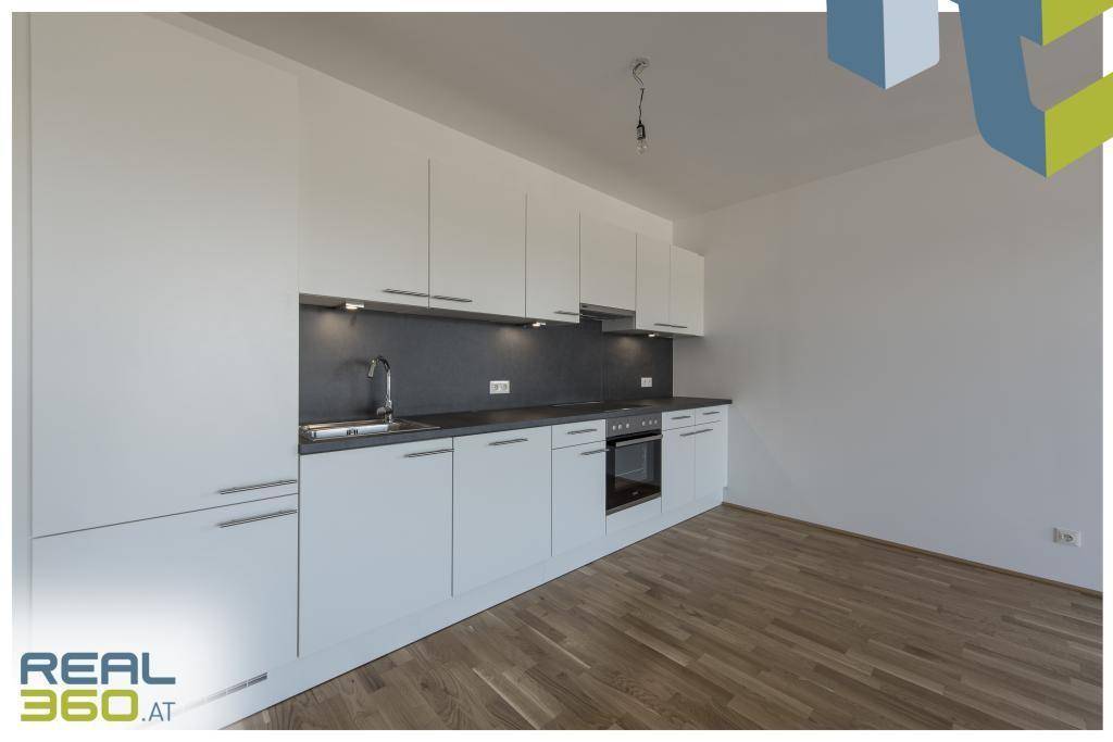 Moderne Einbauküche mit weißen Schränken, dunkler Arbeitsplatte und integriertem Backofen.