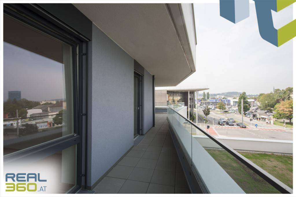 Langer Balkon mit Fliesenboden und Glasgeländer, bietet einen Blick auf die Straße.