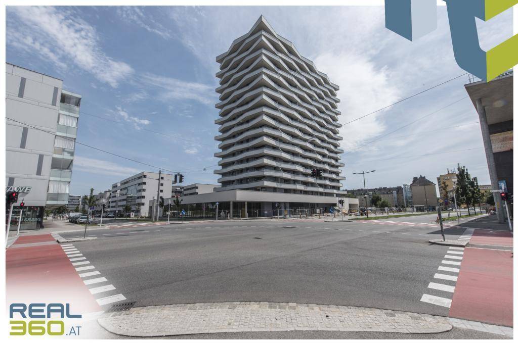 Modernes Wohngebäude an einer städtischen Kreuzung mit umliegenden Gebäuden und Straßen.