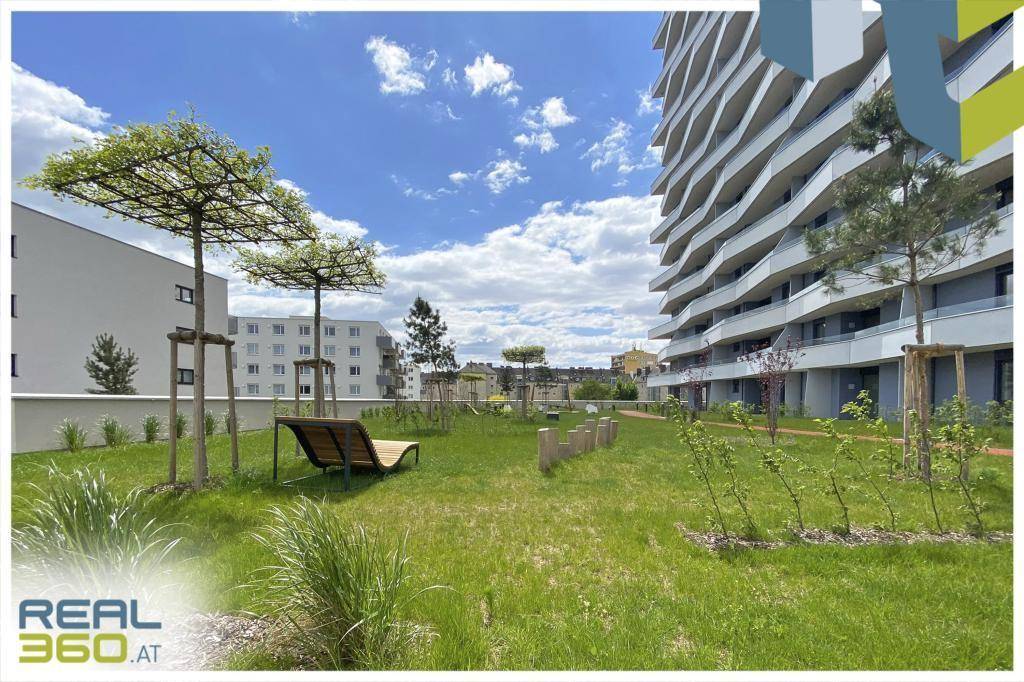 Gemeinschaftlicher Gartenbereich mit Rasenfläche, jungen Bäumen und einer Holzliege.