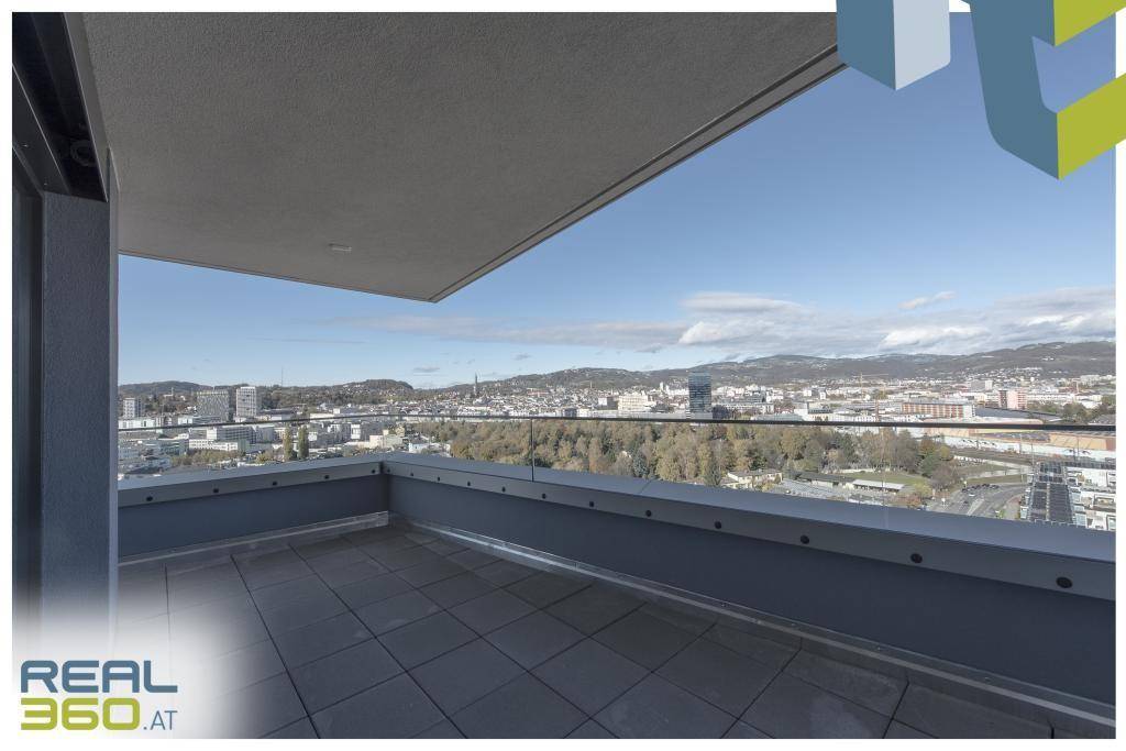 Große Terrasse mit Fliesenboden und Glasgeländer, bietet einen weiten Stadt- und Bergblick.