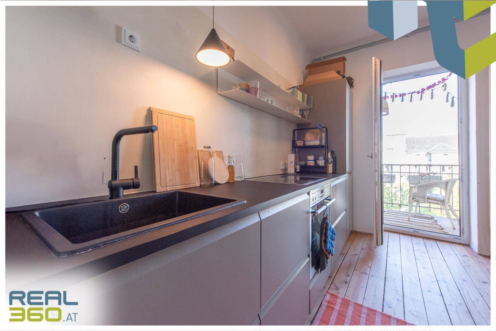 Moderne Küche mit dunkler Arbeitsplatte, Spüle und direktem Zugang zum Balkon.