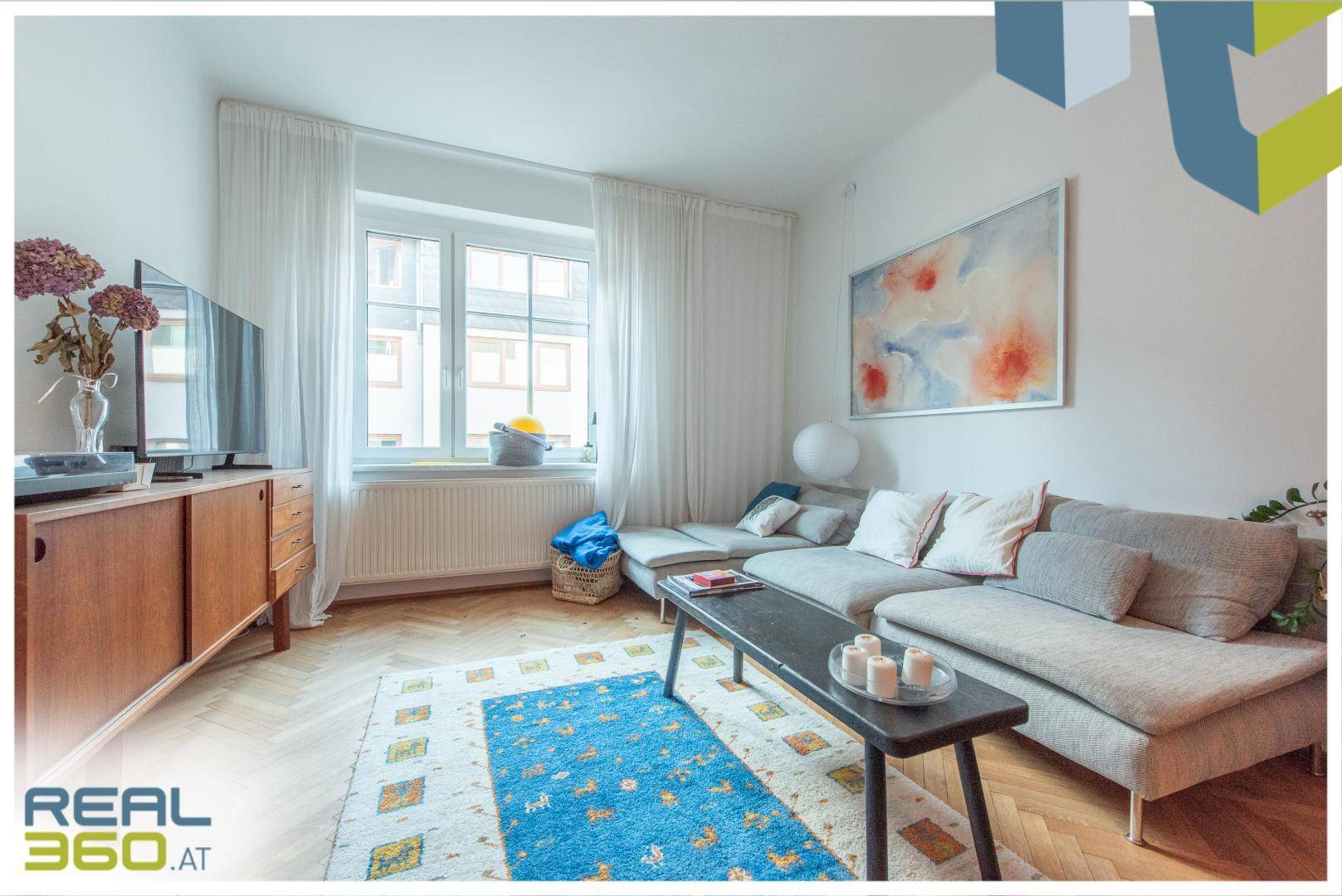 Gemütliches Wohnzimmer mit großem Sofa, Fernseher und hellem Fischgrätparkettboden.