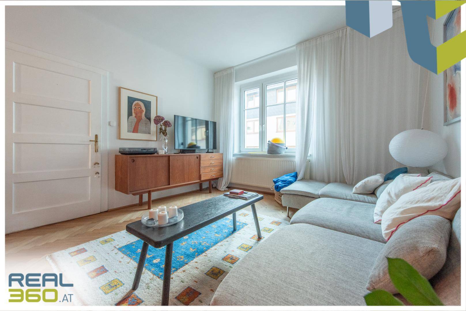 Wohnzimmer mit hellem Fischgrätparkett, bequemer Couch und stilvollem Sideboard.