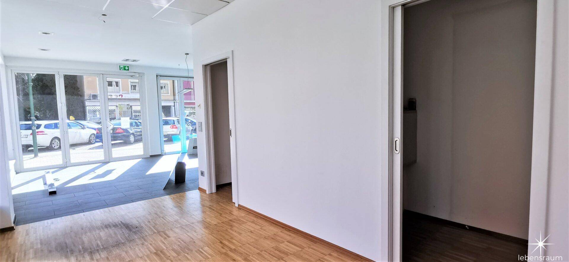 Heller Büroraum mit Holzparkett und großen Fenstern, die viel Tageslicht hereinlassen.