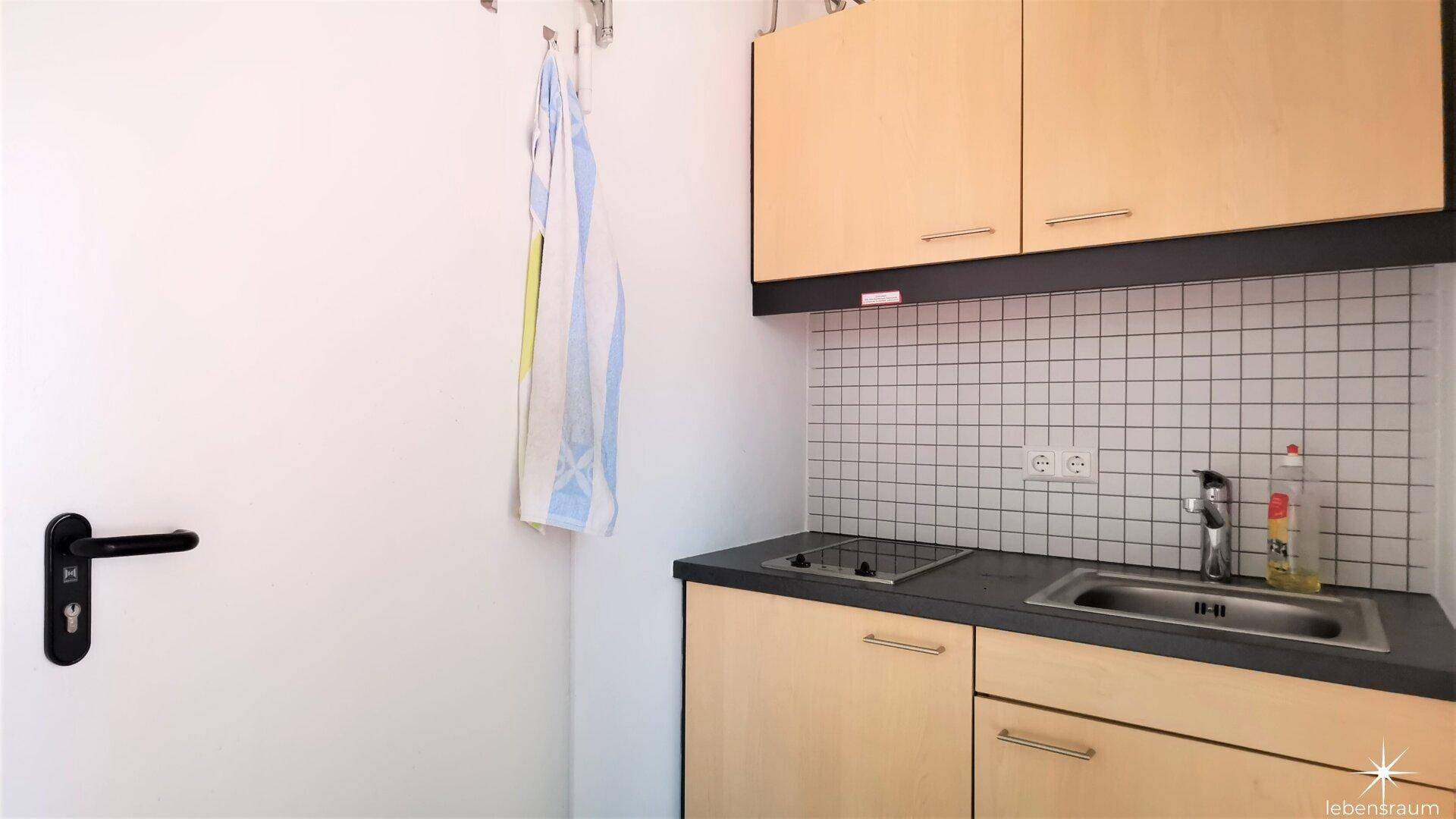 Kompakte Küchenzeile mit Spüle, Kochfeld und Oberschränken, ideal für kleine Büros.