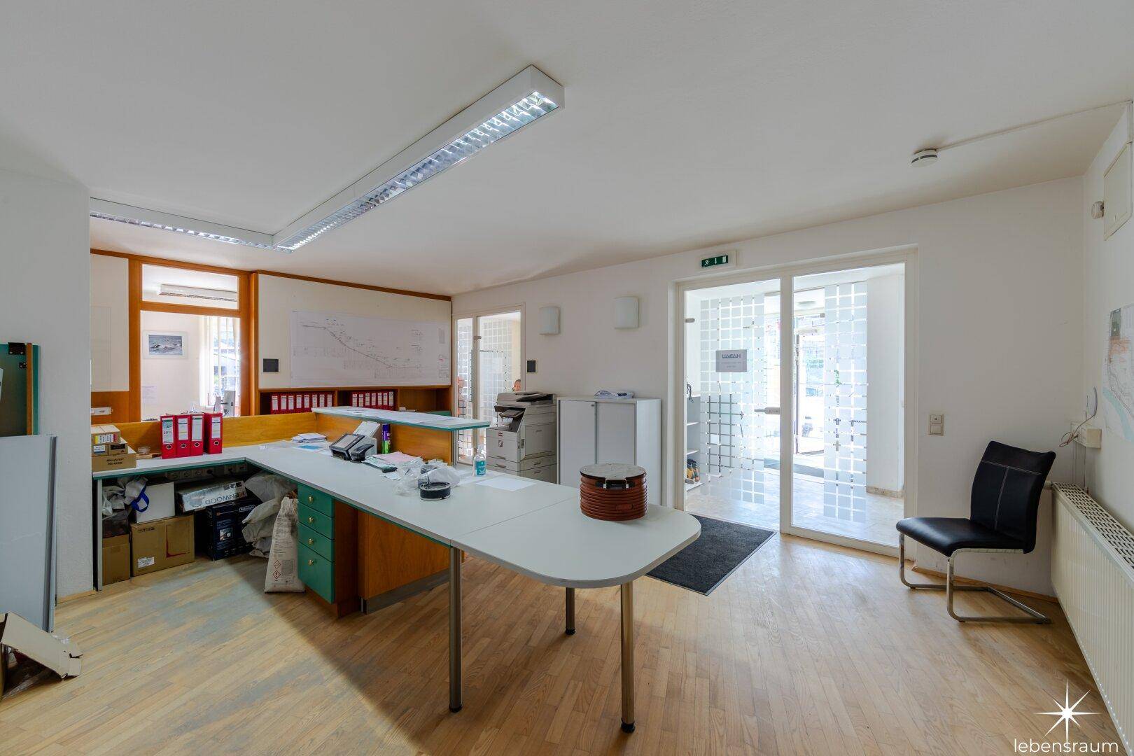 Helles Büro mit Holzboden, Glastüren und einem Empfangstresen im Vordergrund des Raumes.