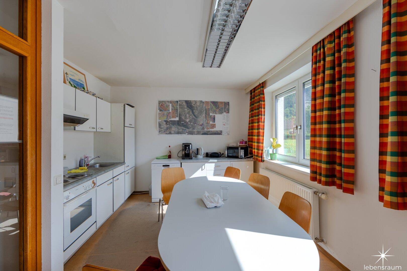 Funktionale Küche mit weißer Einbauküche, Esstisch und Fenster mit Blick ins Grüne.