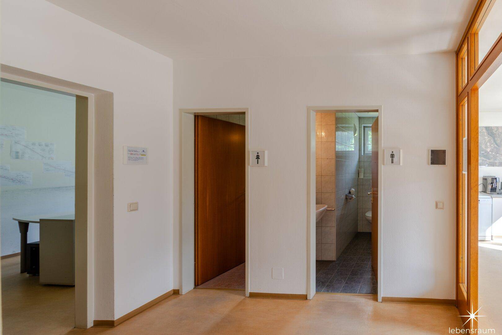 Flur mit Zugang zu zwei Toilettenräumen und einem Blick in die angrenzende Küche.