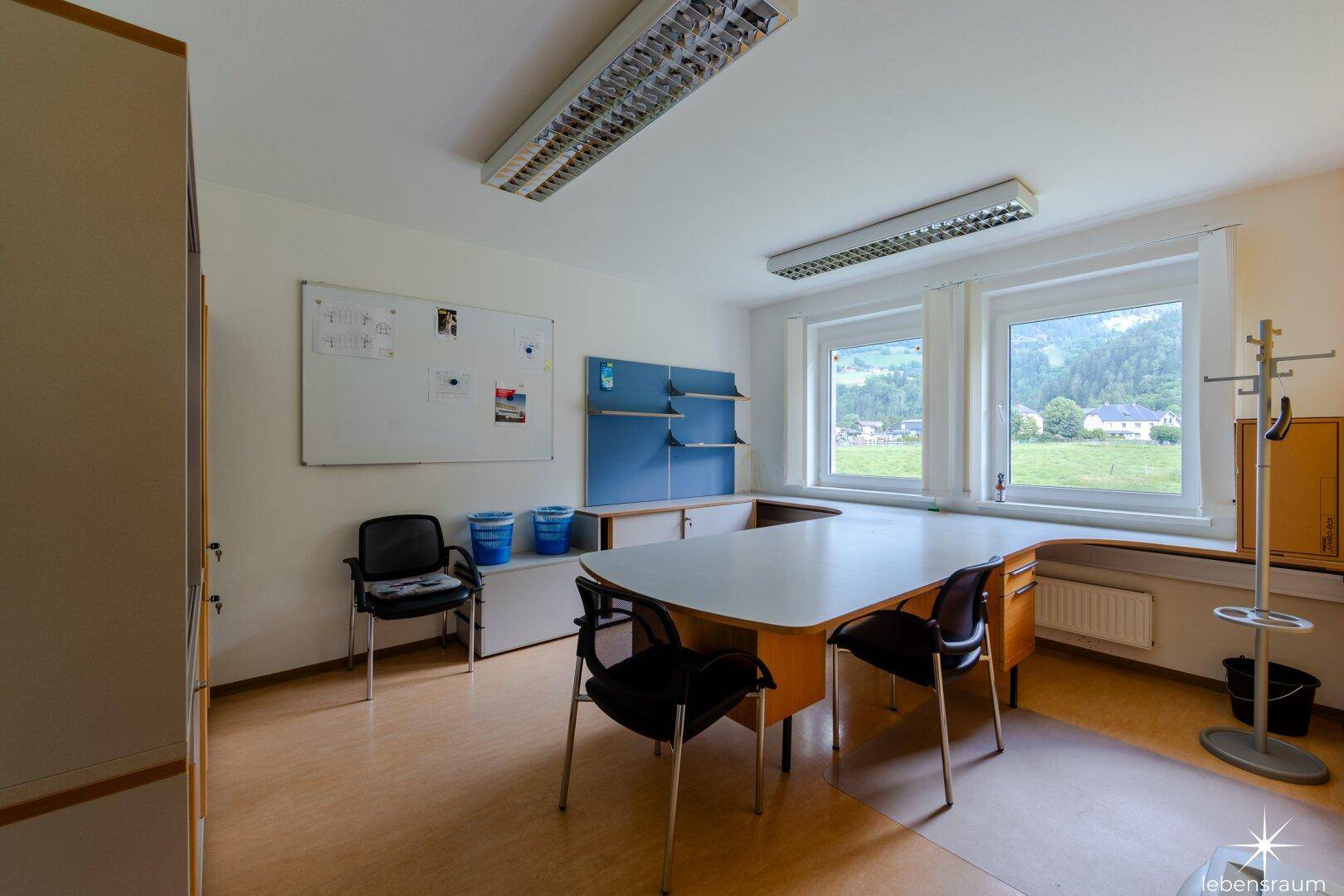Büro mit großem Schreibtisch, Bürostühlen und einem Fenster mit Blick ins Grüne.