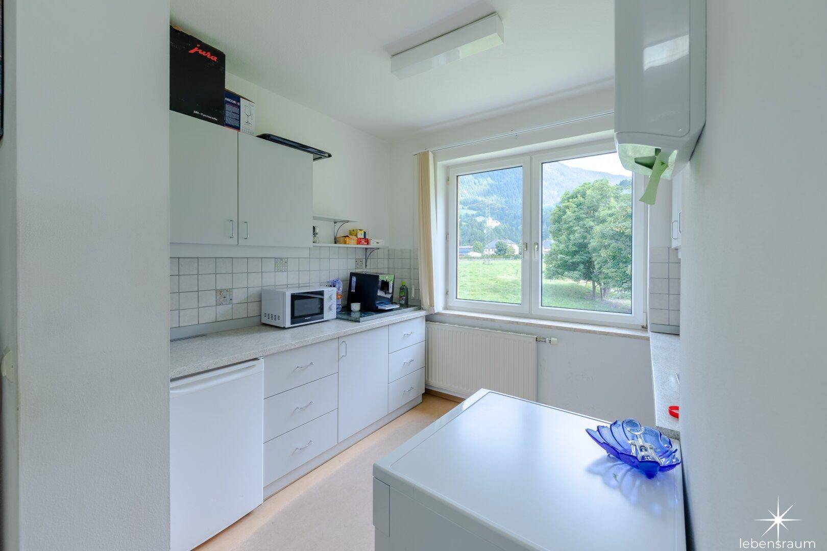 Kleine Küche mit weißen Schränken, Mikrowelle und einem Fenster mit Bergblick.
