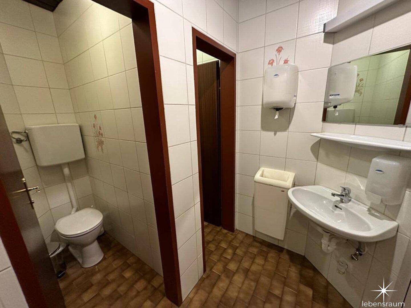Saubere Gästetoilette mit Waschbecken, Spiegel und weißen Fliesen.