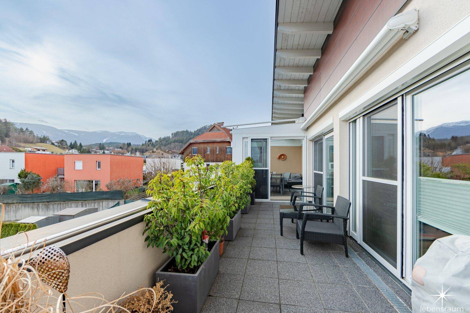 Große geflieste Terrasse mit Sitzgelegenheiten und Pflanzen, mit Blick auf die umliegende Landschaft.
