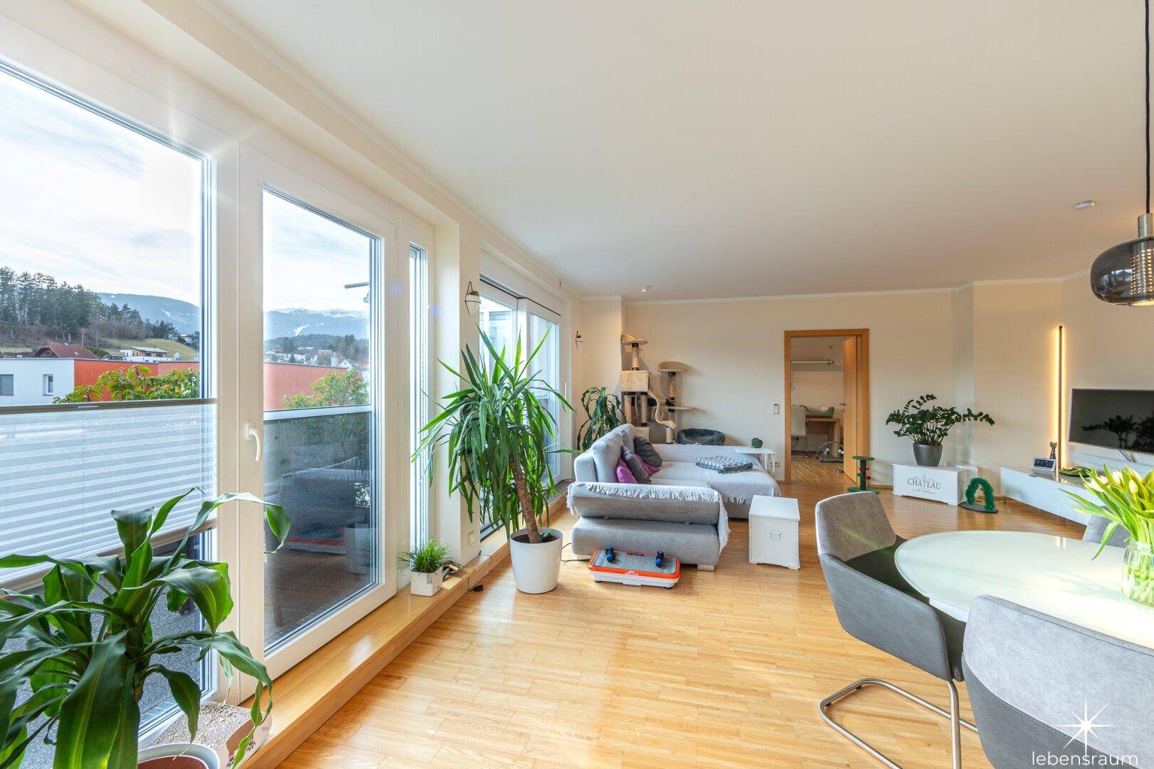 Heller Wohn- und Essbereich mit großen Fenstern, Parkettboden und Zugang zur Terrasse.