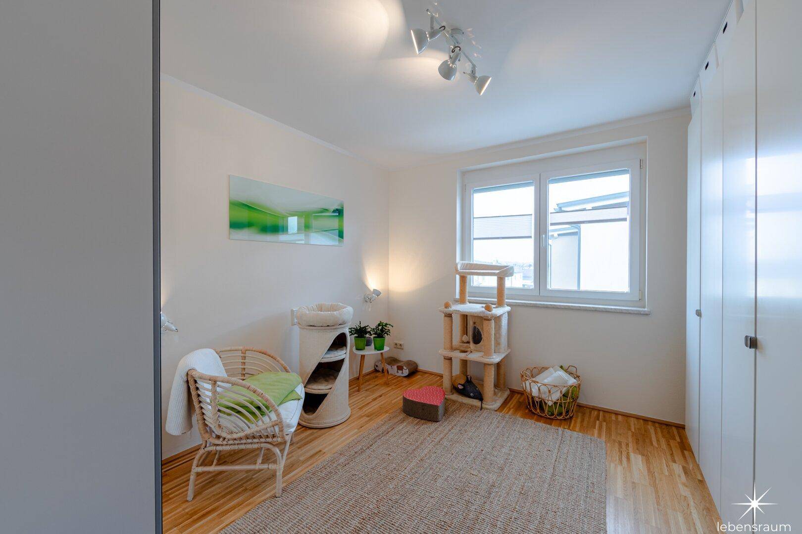 Helles Schlafzimmer mit Parkettboden und großem Fenster, modern und freundlich gestaltet.