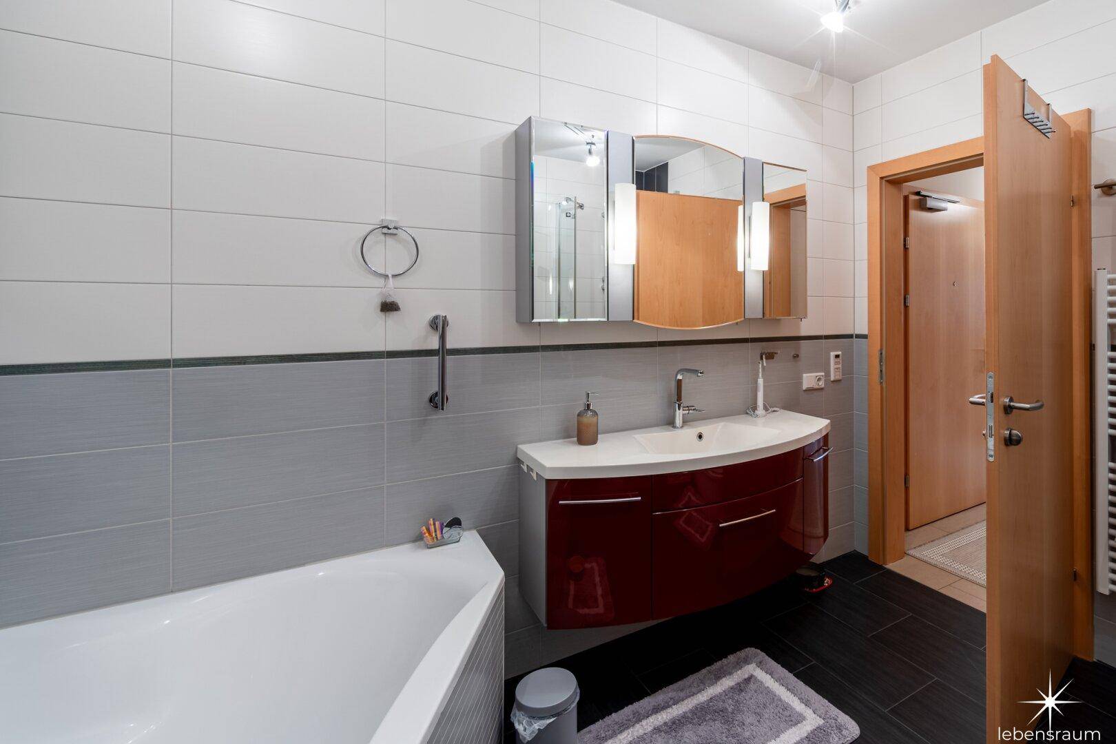 Badezimmer mit Waschtisch, Badewanne und Spiegelschrank, in hellen und dunklen Tönen.