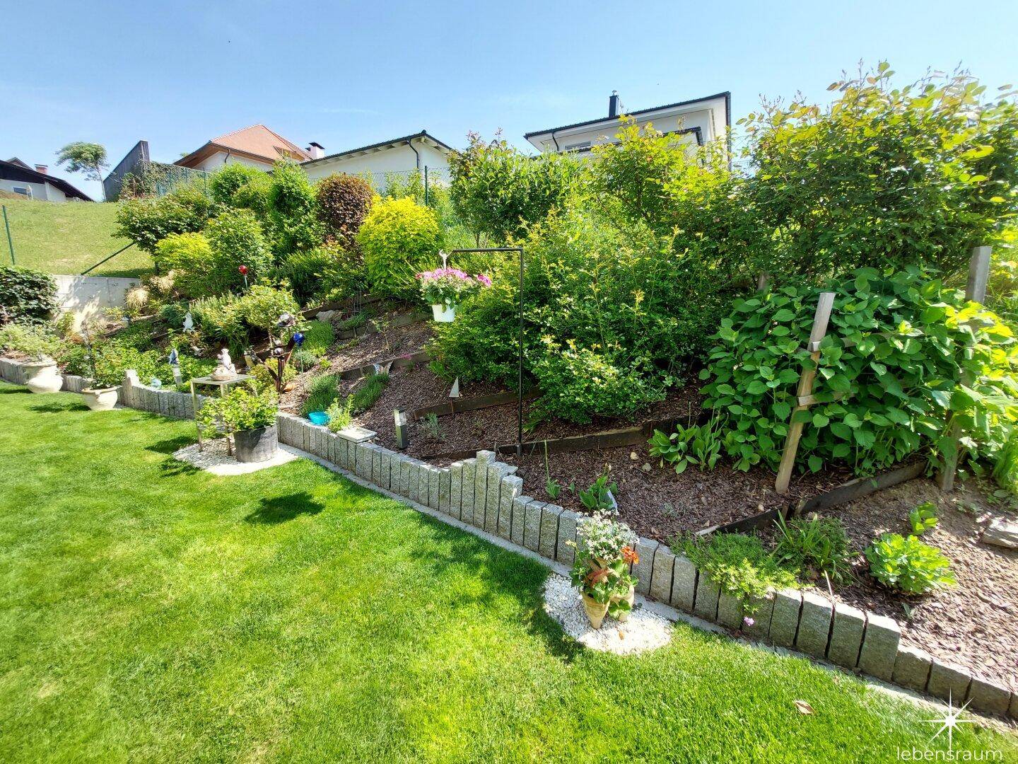 Terrassierter Gartenbereich mit üppiger Bepflanzung und Steinmauern, gut gepflegt.