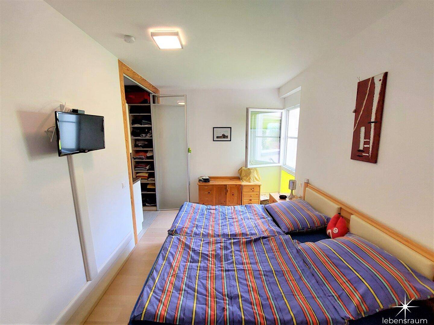 Helles Schlafzimmer mit Doppelbett, Holzboden und Zugang zum begehbaren Kleiderschrank.