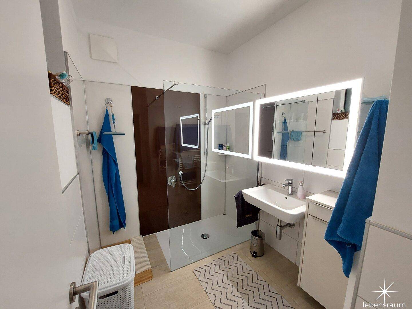 Modernes Badezimmer mit ebenerdiger Dusche, beleuchtetem Spiegel und eleganten Fliesen.