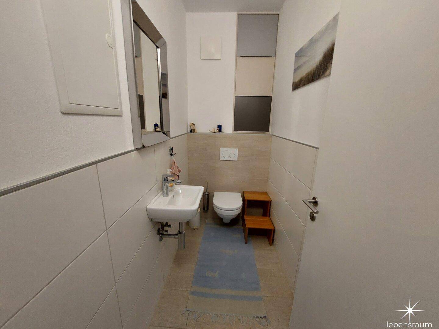 Gäste-WC mit wandhängendem WC, kleinem Waschbecken und modernen Fliesen.