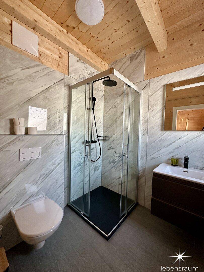 Modernes Badezimmer mit Duschkabine, WC, Waschbecken und Marmoroptik-Fliesen.