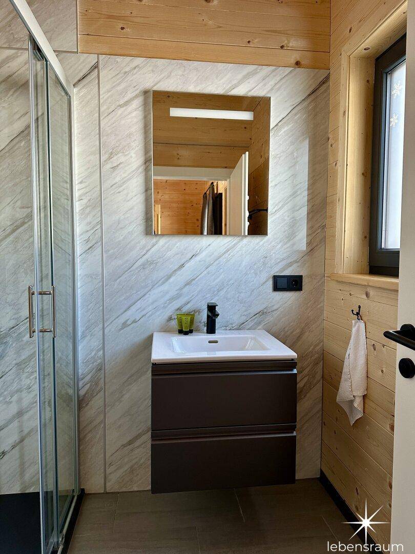 Waschbeckenbereich im Badezimmer mit Spiegel, Holzwänden und modernen Fliesen.